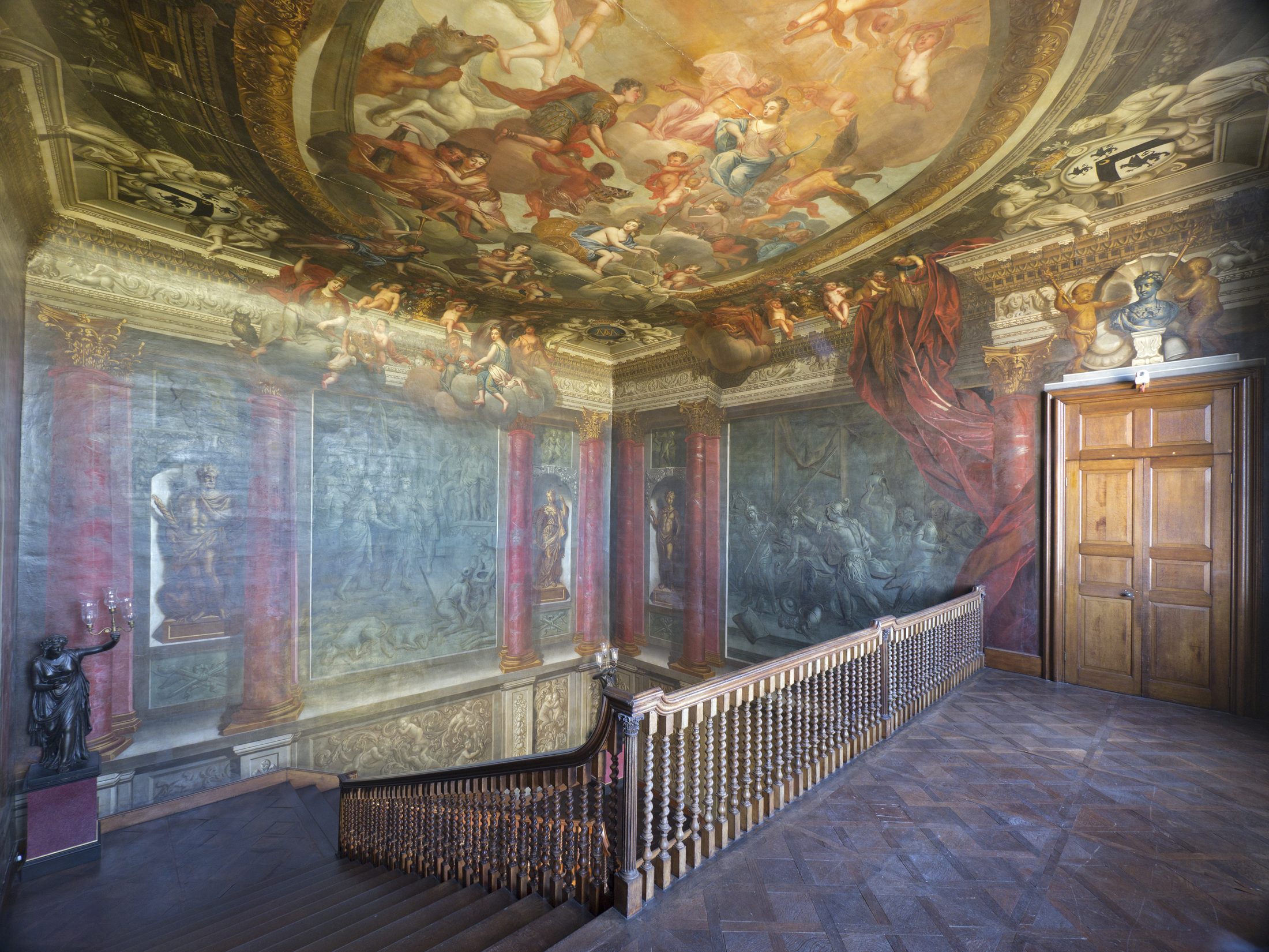 The top landing of the Great Stair, beneath Lanscroon's painted ceiling, with the grisaille wall murals and red scagliola columns